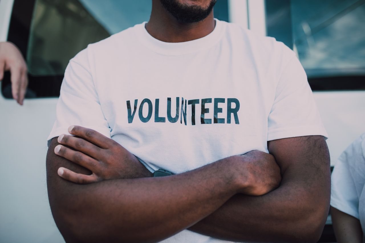 Free A close-up of a person wearing a volunteer shirt with arms crossed, promoting community service. Stock Photo