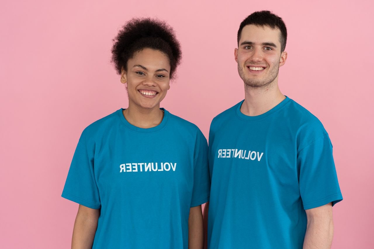 Free Two volunteers wearing t-shirts pose cheerfully against a pink studio background. Stock Photo